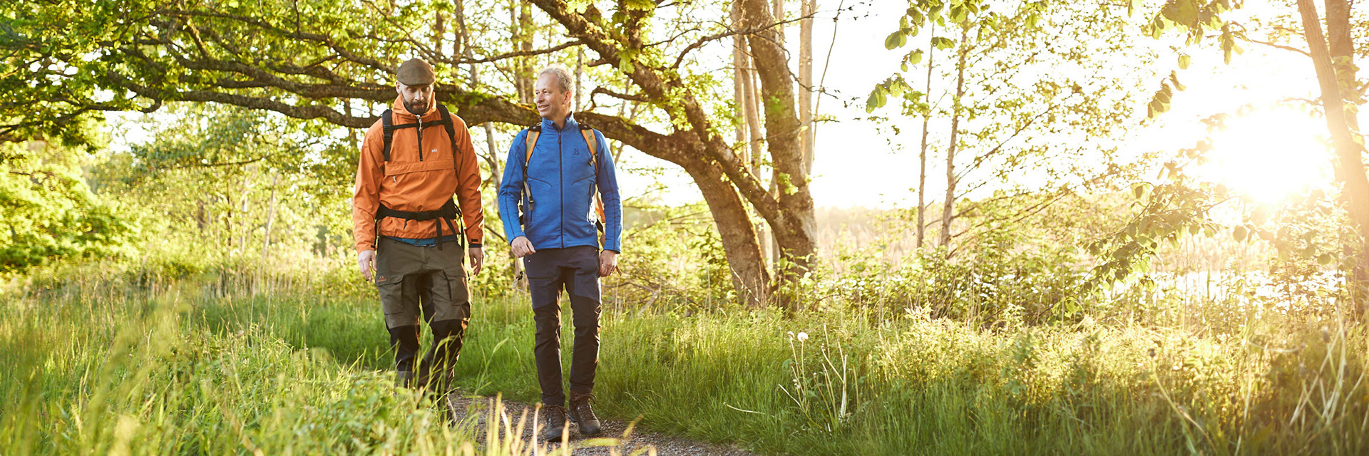 Två män går på grusstig i lövskog.