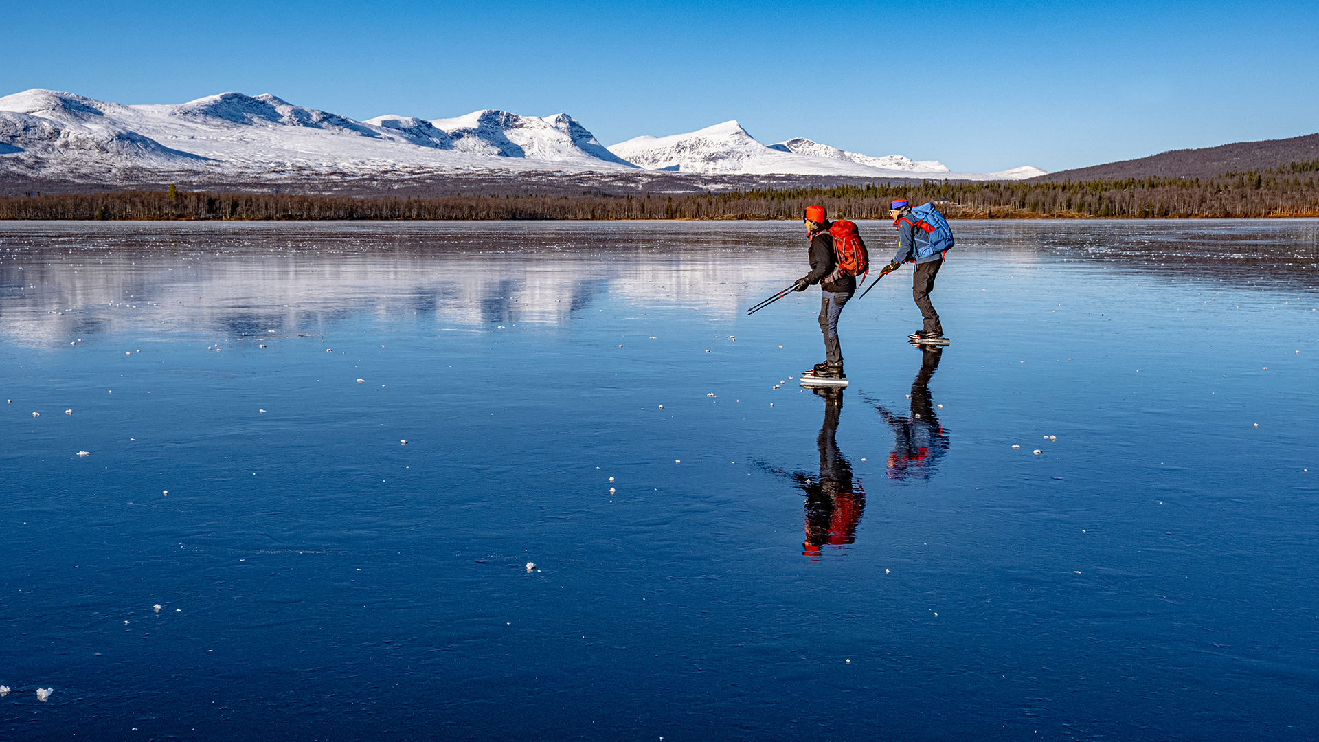 Fotograf: Naturvårdsverket. Två personer åker skridskor på blankis med fjällen i bakgrunden.