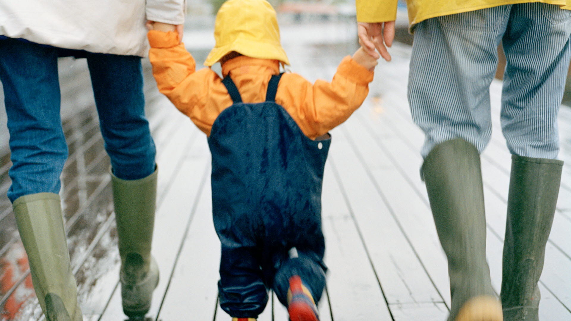 Ett barn som går mellan sina föräldrar i regnet. Sandhamn Stockholms skärgård