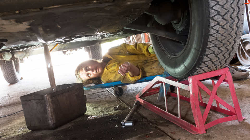 Kvinna ligger under bil och tömmer den på olja