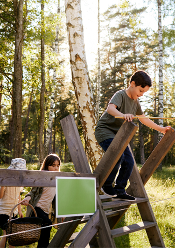 Barn på utflykt i skogen med fjärilshåvar och picknickkorg. De klättrar över ett stängsel vid en stätta (en form av trappa över stängslet).
