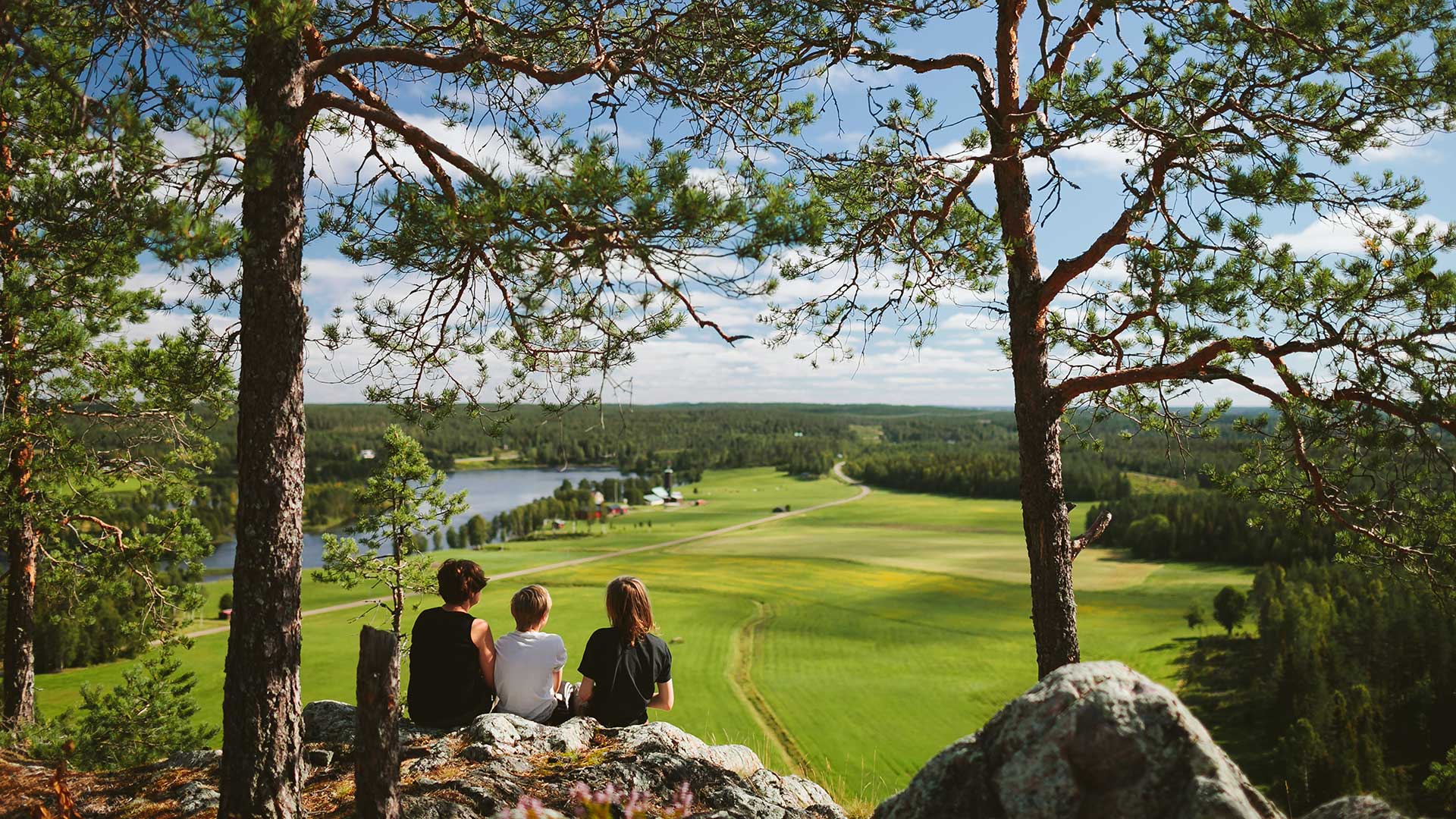 Fotograf: Matilda Holmqvist
Bildbyrå: Johnér Tre personer sitter på en höjd (Falkberget) och ser ut över ett odlingslandskap med en sjö
