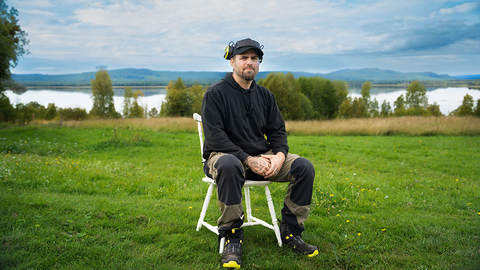 Anders sitter på en stol med en sjö och fjäll i bakgrunden