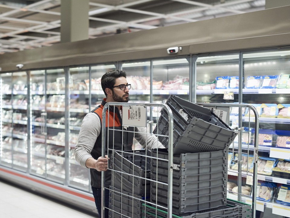 En anställd i en livsmedelsbutik skjuter en vagn med plastbackar framför sig
