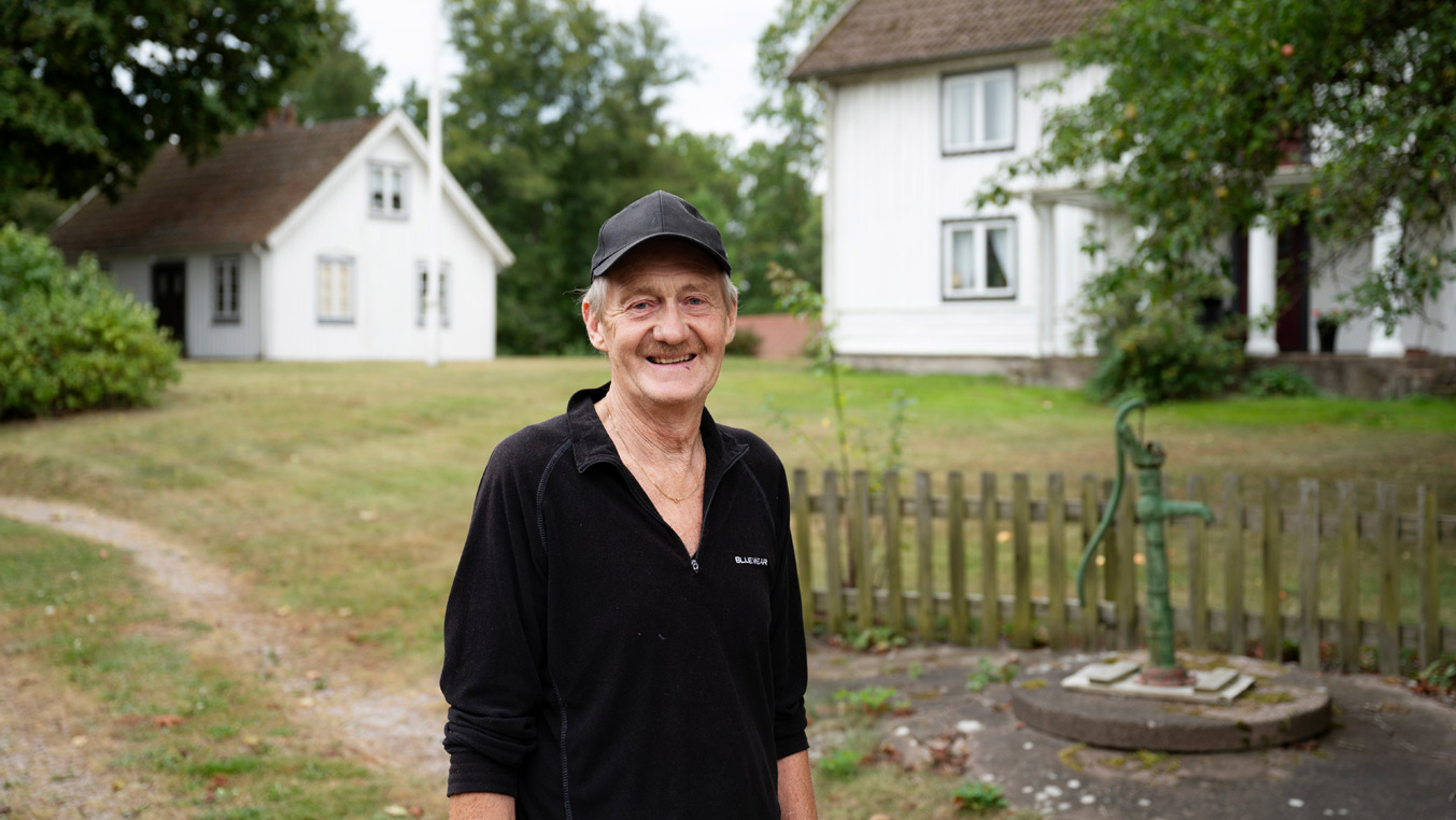 Fotograf: Lina Alriksson Porträtt av en man framför två vita hus och en gammal vattenpump