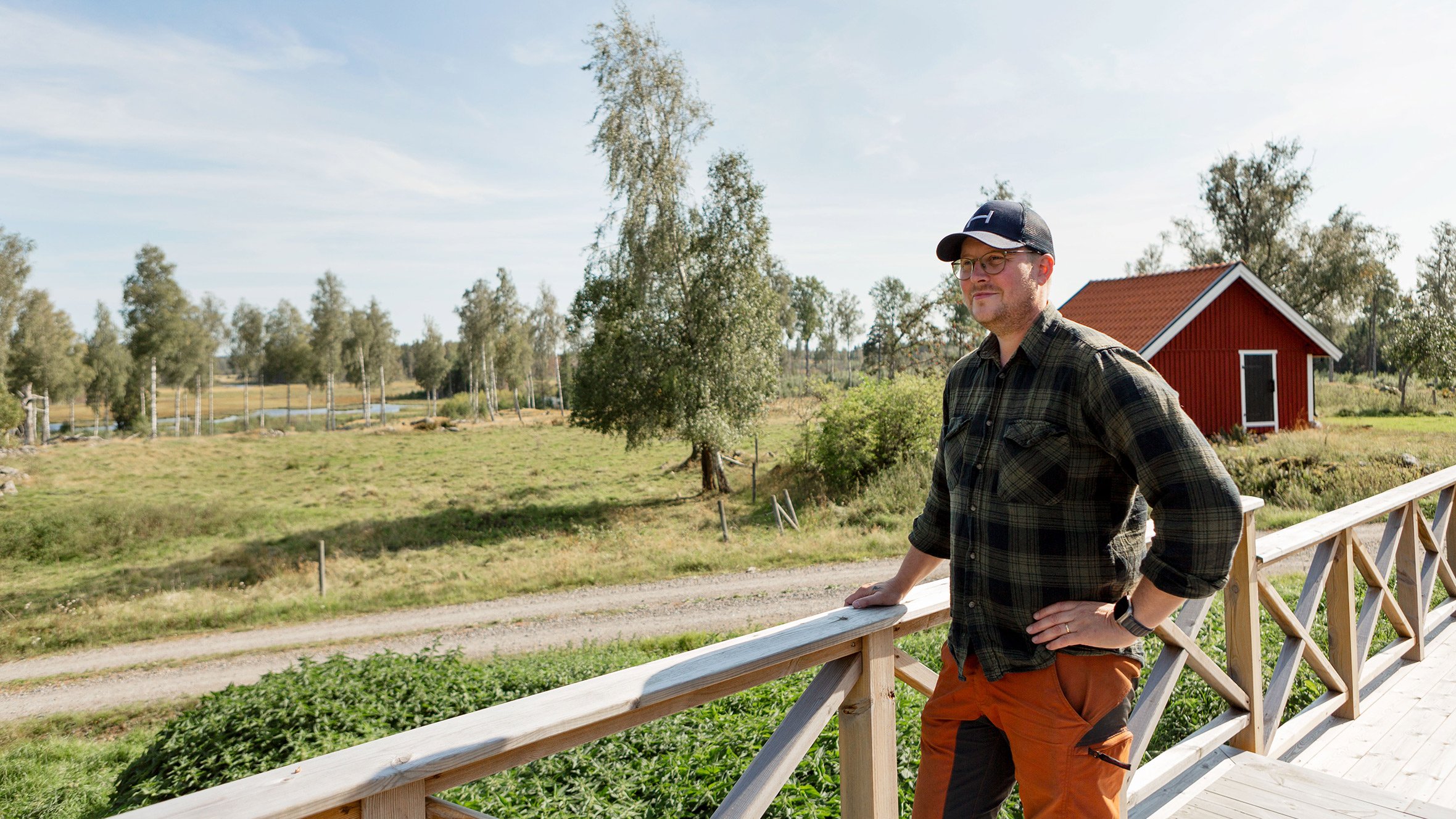 Fotograf: Lisa Öberg Man på trädäck som blickar ut över gård och grönska