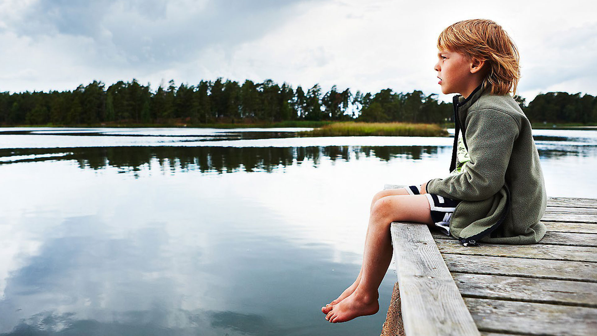En pojke sitter på en brygga och blickar ut över en sjö.
