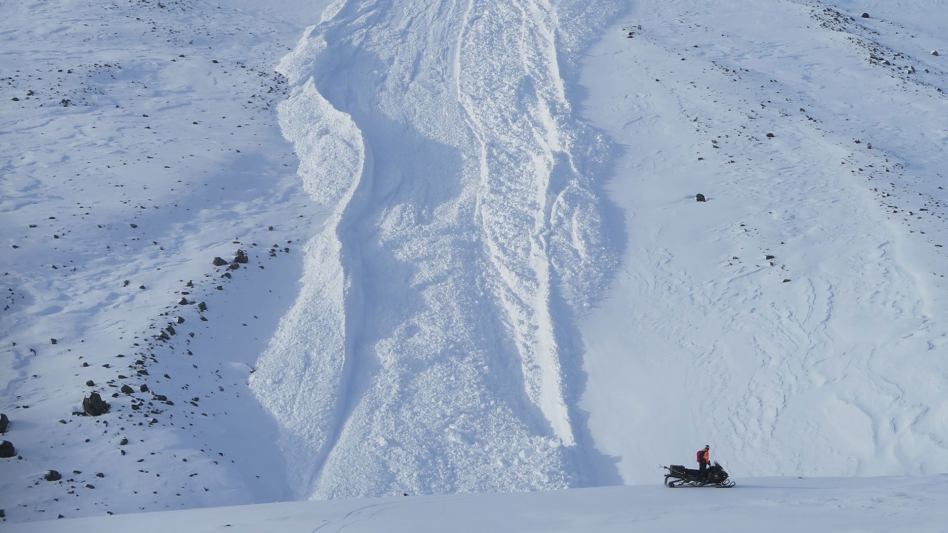 En snöskoter framför ett snötäckt berg.