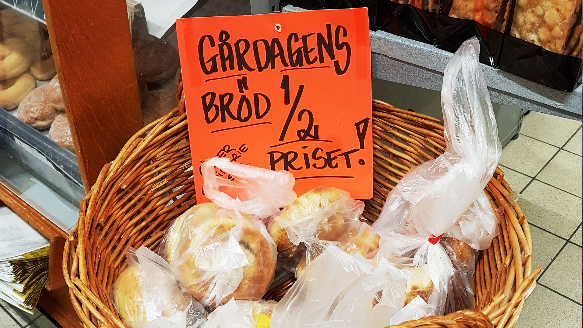 En skylt "gårdagens bröd halva priset" i en korg med bröd.