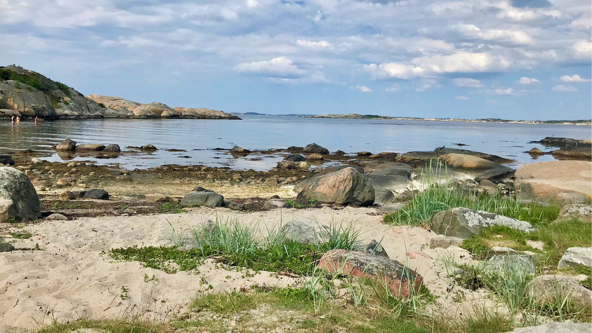 Fotograf: Malin Gustafsson. Havsvik med sanddyner och badande människor i bakgrunden.