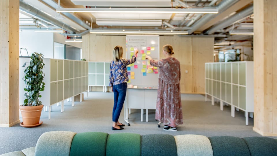 Två personer sätter upp post it-lappar på en whiteboard.