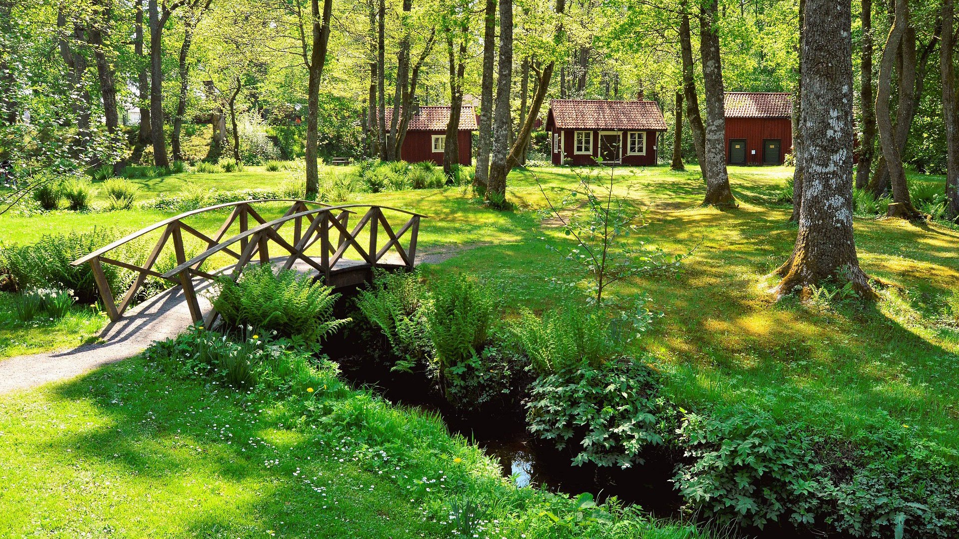 Fotograf: Jonathan Petersson
Bildbyrå: Pixabay Liten träbro över bäck i skogslandskap med röda små hus i bakgrunden