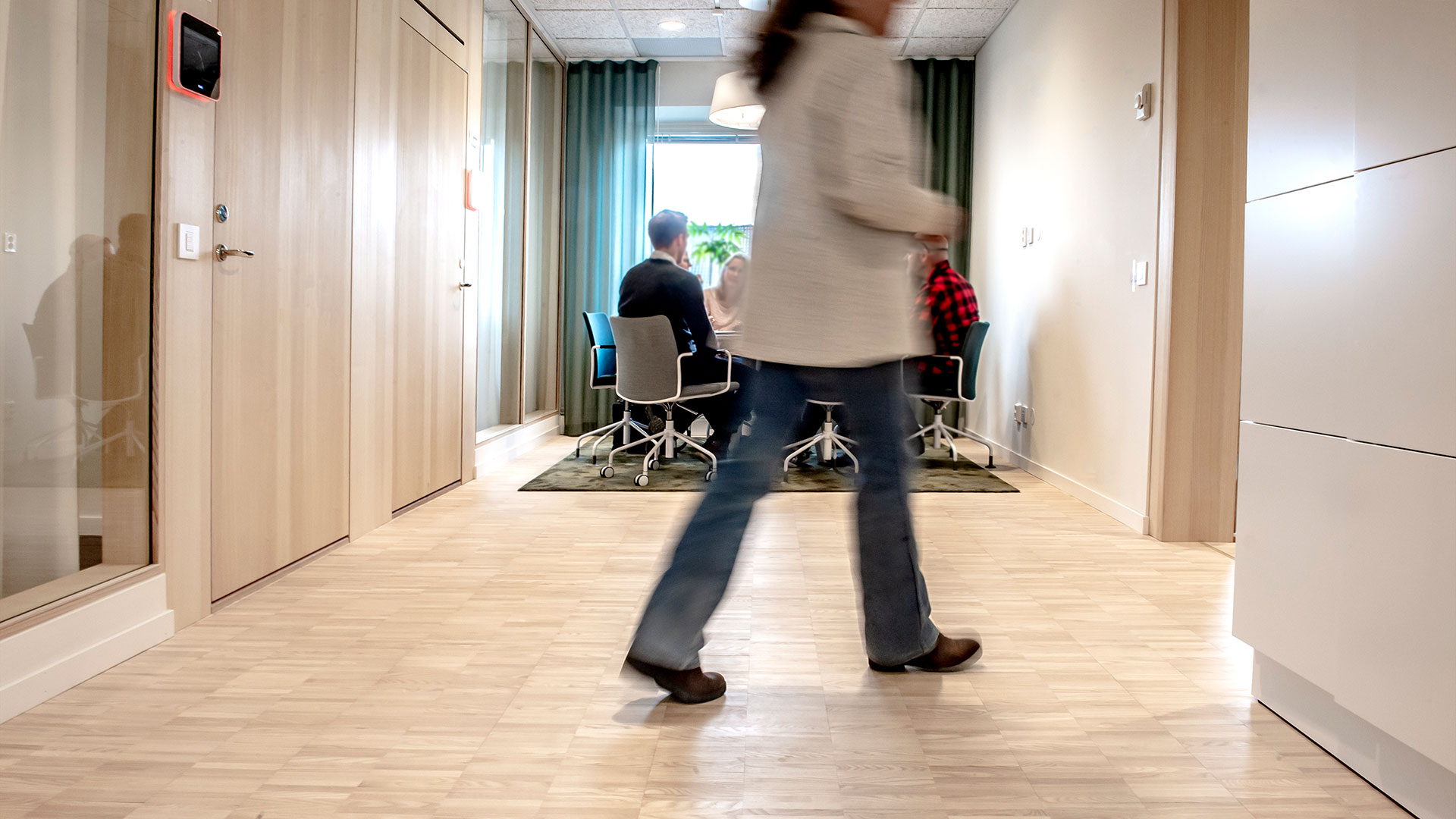 En person går förbi ett konferensrum där några personer sitter i möte.