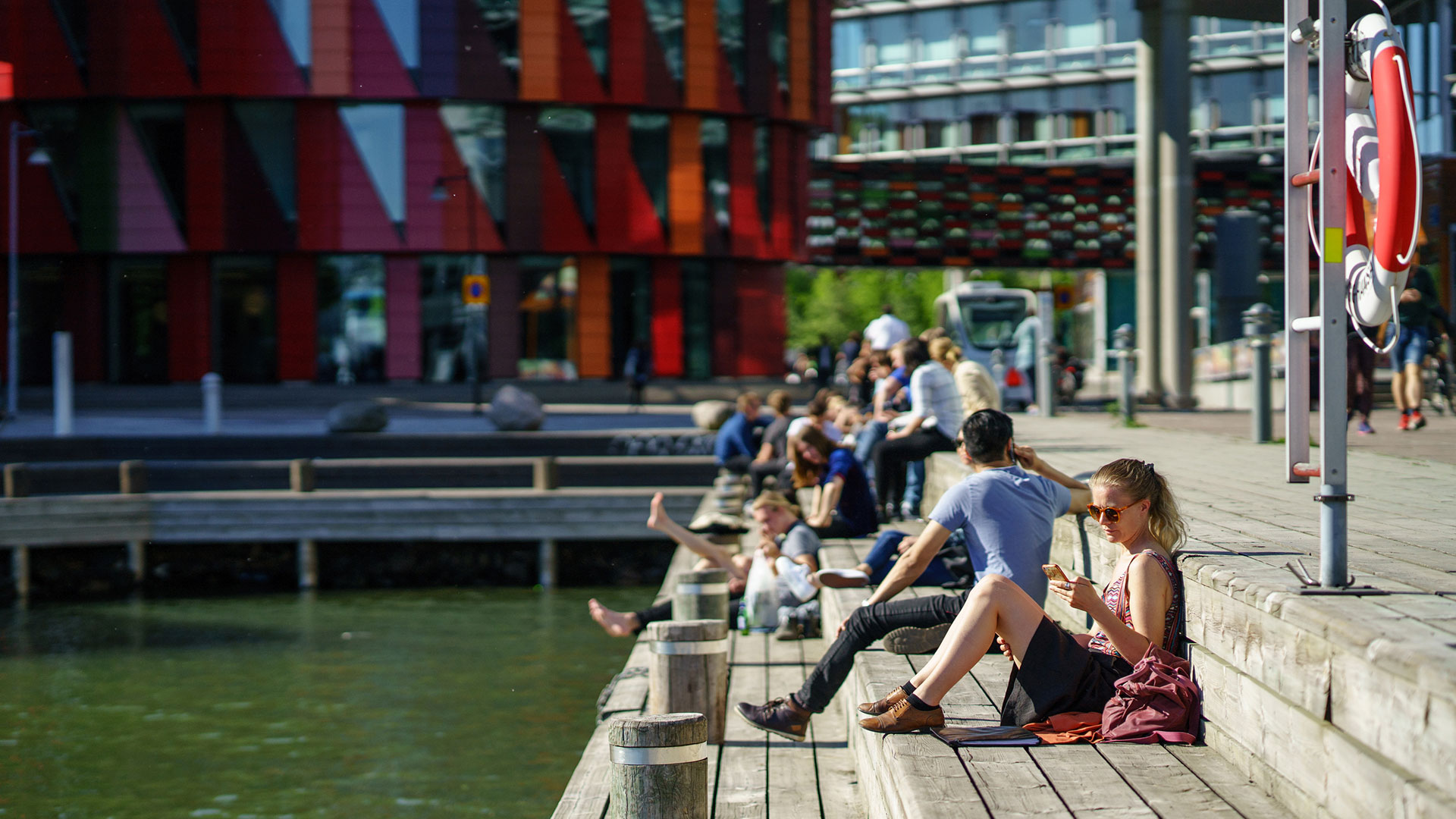 Människor njuter av solskenet i Lindholmens hamn.
