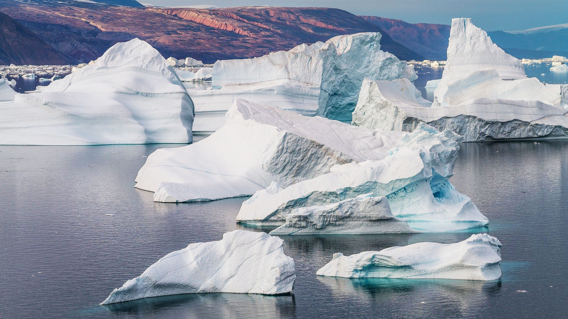 Isberg på Grönland, i bakgrunden fjäll i solljus. 