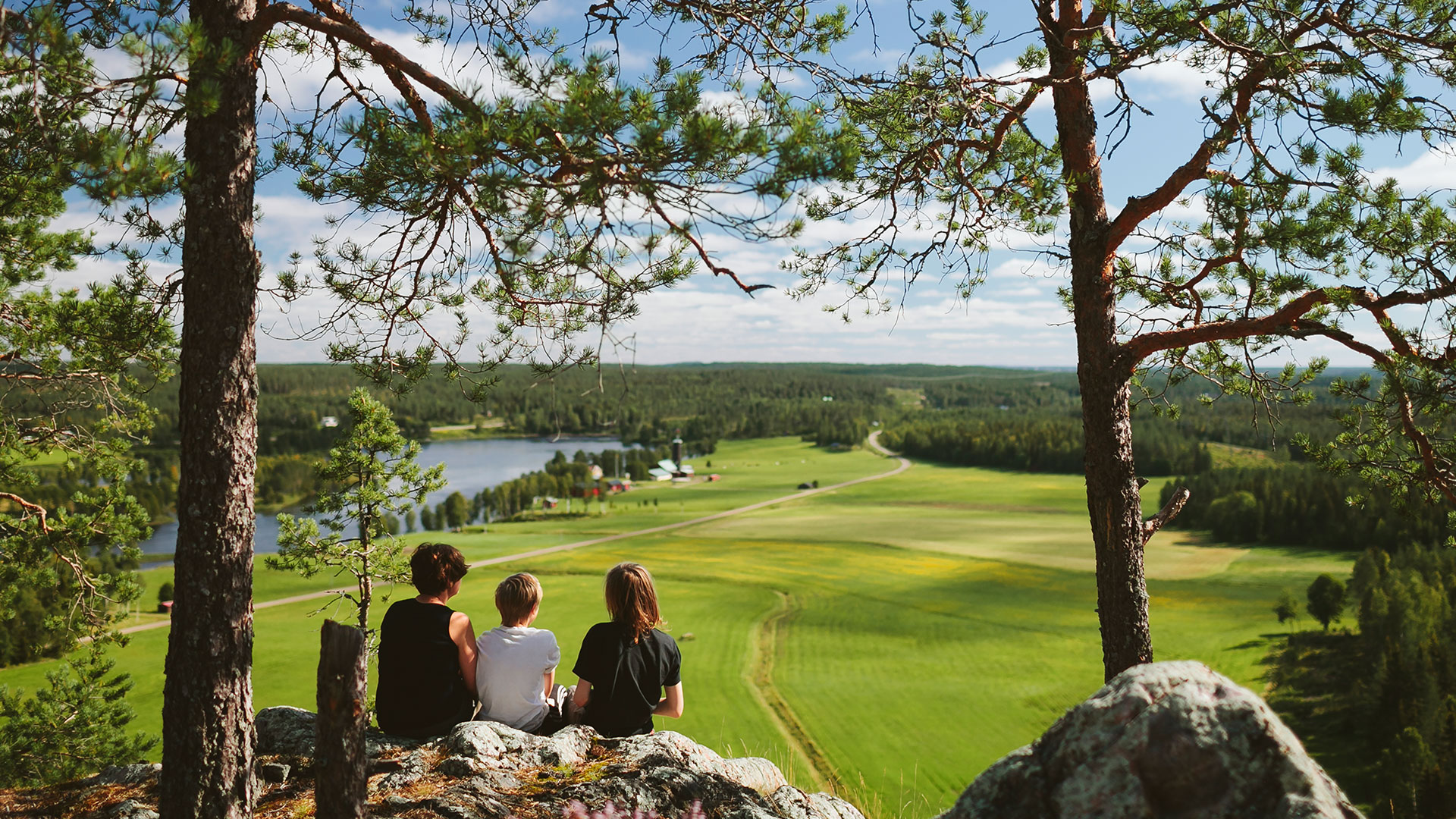 Fotograf: Matilda Holmqvist
Bildbyrå: Johnér Tre personer sitter på en höjd (Falkberget) och ser ut över ett odlingslandskap med en sjö.